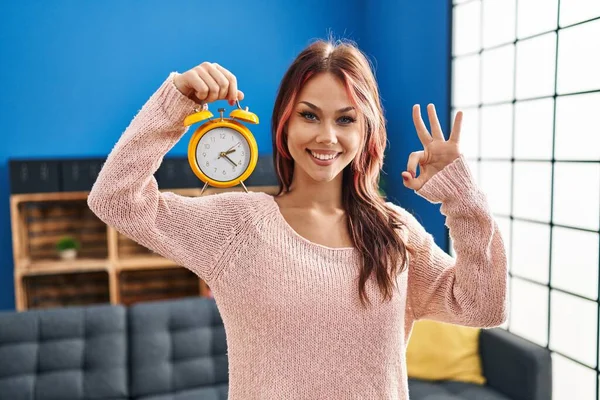 Young Caucasian Woman Holding Alarm Clock Doing Sign Fingers Smiling — Stock Photo, Image