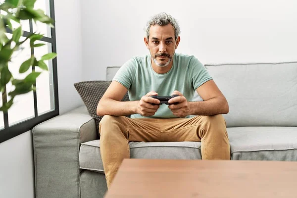 中年时 他的惊慌失措的男人坐在沙发上玩电子游戏 态度和表情看起来很自信 — 图库照片