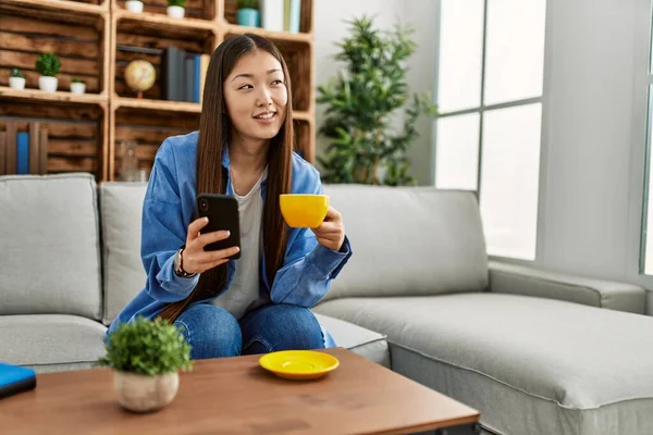 Giovane Ragazza Cinese Utilizzando Smartphone Bere Caffè Seduto Sul Divano — Foto Stock