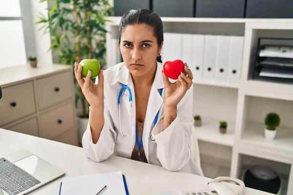 Young Hispanic Woman Working Dietitian Clinic Holding Green Apple Skeptic —  Fotos de Stock