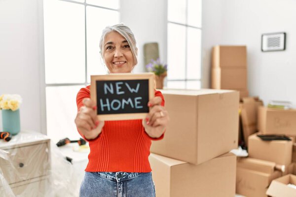 Middle age grey-haired woman smiling confident holding new home blackboard at new home