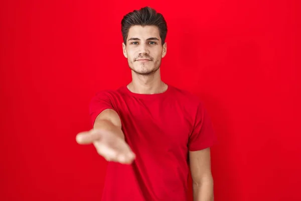Mladý Hispánec Muž Stojící Nad Červeným Pozadím Úsměvem Veselá Nabídka — Stock fotografie