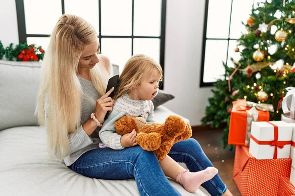 妈妈和女儿在家里的圣诞树旁梳头 — 图库照片