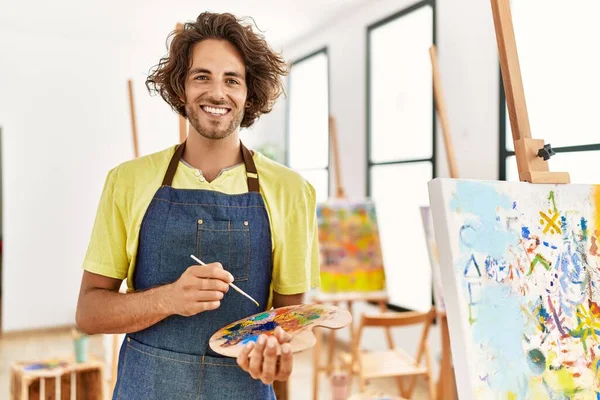 Młody Latynos Artysta Człowiek Uśmiecha Szczęśliwy Trzymając Pędzel Paletę Studio — Zdjęcie stockowe