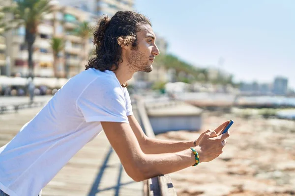Young Hispanic Man Using Smartphone Serious Expression Seaside — Stock Photo, Image