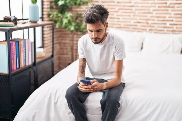 Young Hispanic Man Using Smartphone Sitting Bed Bedroom — стоковое фото