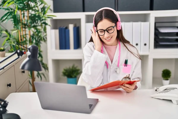 Young woman wearing doctor uniform listening to music working at clinic