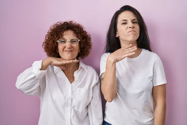 西班牙裔母亲和女儿穿着宽松的白色T恤 手拿着刀在粉色背景下割喉 扬言要大动干戈 — 图库照片
