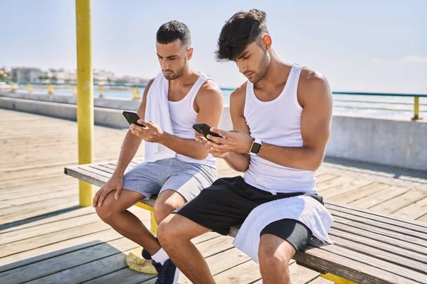 Dos Hombres Hispanos Pareja Deportiva Usando Teléfono Inteligente Sentado Banco —  Fotos de Stock
