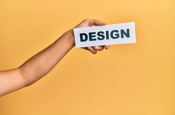 Hand of caucasian man holding paper with design word over isolated yellow background