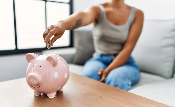 Young Hispanic Woman Inserting Coin Piggy Bank Home — 스톡 사진