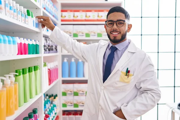 Молодий Латинський Чоловік Фармацевт Посміхається Впевнено Тримає Продукт Стелажах Аптеці — стокове фото