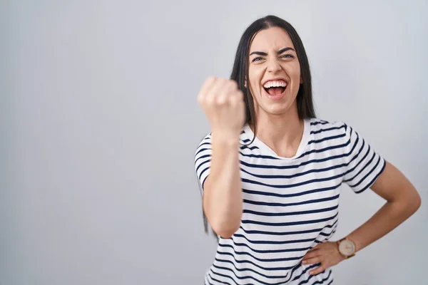 縞模様のTシャツを着た若いブルネットの女性は怒りで叫んでいる間に怒りと怒りに苛まれ 激怒して拳を上げる 怒りと攻撃的な考え方 — ストック写真