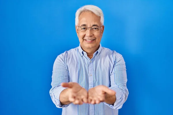 Hispanic senior man wearing glasses smiling with hands palms together receiving or giving gesture. hold and protection