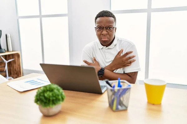 Young african man working at the office using computer laptop shaking and freezing for winter cold with sad and shock expression on face