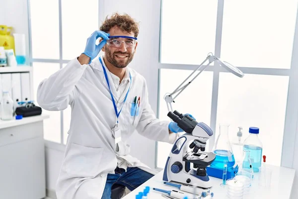 研究室で顕微鏡を使って科学者の制服を着た若いヒスパニック系の男 — ストック写真