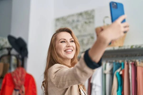 年轻的金发女顾客在服装店的智能手机旁自拍 — 图库照片