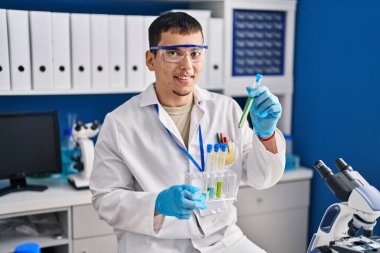 Young man scientist smiling confident holding test tubes at laboratory