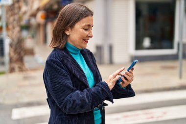 Sokakta akıllı telefon kullanan orta yaşlı bir iş kadını.