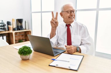 Ofiste çalışan son sınıf öğrencisi bilgisayarla gülümseyen parmaklarını zafer işareti yaparken gösteren kameraya bakıyor. İki numara.. 