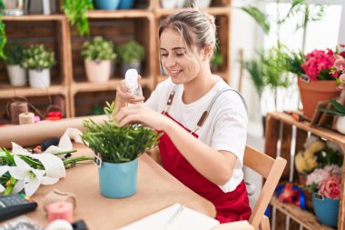 Young blonde woman florist using diffuser working at flower shop