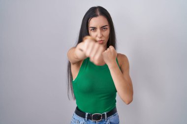 İzole edilmiş arka planda duran genç bir kadın dövüşmek için yumruk atıyor, agresif ve kızgın saldırı, tehdit ve şiddet. 