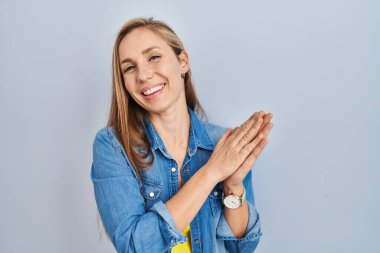 Mavi arka planda duran genç sarışın kadın alkışlıyor ve alkışlıyor mutlu ve neşeli, gururlu elleri bir arada. 