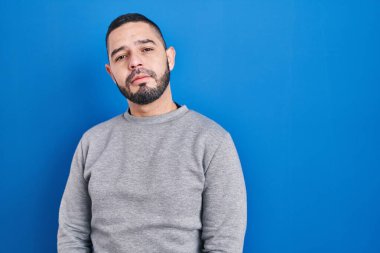 Mavi arka planda duran İspanyol adam yüzünde ciddi bir ifadeyle rahatlamış. Basit ve doğal bir şekilde kameraya bakıyorsun.. 