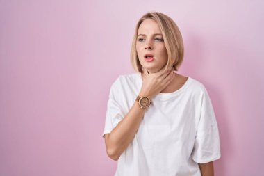 Pembe arka planda duran beyaz bir kadın ağrılı bir boyuna dokunuyor, grip, mantar ve enfeksiyon yüzünden boğaz ağrısı çekiyor. 