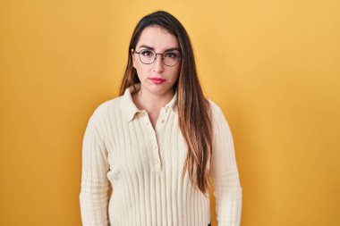Young hispanic woman standing over yellow background relaxed with serious expression on face. simple and natural looking at the camera. 