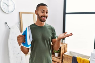 African american man holding electric iron celebrating achievement with happy smile and winner expression with raised hand 