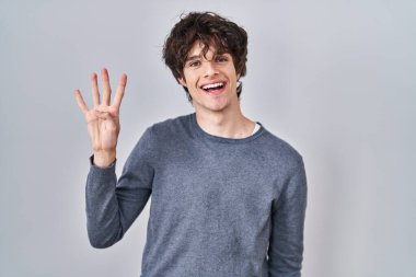 İzole edilmiş arka planda duran genç adam, kendinden emin ve mutlu gülümserken dört numarayı gösteriyor ve işaret ediyor.. 