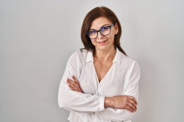 Orta yaşlı İspanyol kadın izole edilmiş arka planda durmuş kollarını kavuşturup kameraya bakarken gülümsüyor. pozitif kişi. 