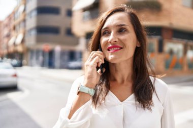 Genç, güzel, İspanyol bir kadın gülümsüyor ve caddede akıllı telefondan konuşuyor.