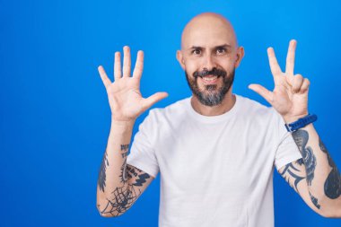 Mavi arka planda dikilen İspanyol dövmeli adam 8 numarayı gösterip işaret ederken kendinden emin ve mutlu gülümsüyor.. 