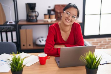 Young chinese woman business worker using laptop sitting with arm crossed gesture at office