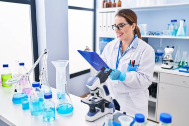 Young beautiful hispanic woman scientist writing report working at laboratory