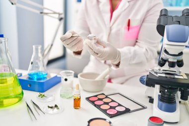 Young hispanic woman wearing scientist uniform mixing powder at laboratory