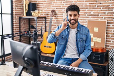 Genç Arap müzisyen gülümsüyor. Müzik stüdyosundaki akıllı telefondan konuşuyor.