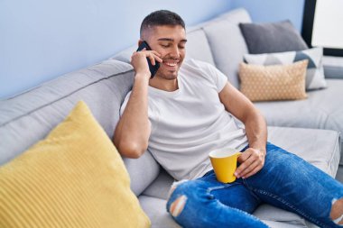 Genç İspanyol adam kahve içiyor ve evde akıllı telefondan konuşuyor.