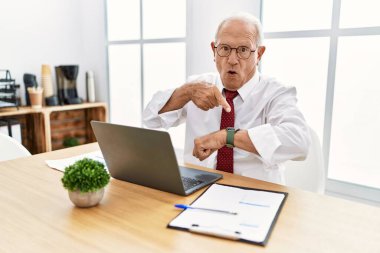 Ofiste çalışan kıdemli bir adam bilgisayarını kullanıyor. Aceleyle saati, sabırsızlığı ve gecikmeyi gösteriyor. 