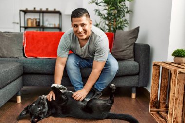 Genç İspanyol gülümseyen adam evde köpekle oynarken mutlu oluyor..