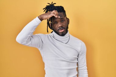 Sarı arka planda balıkçı yaka kazak giyen Afrikalı bir adam alnındaki sivilceden mutsuz olduğunu gösteriyor, siyah noktalı çirkin bir enfeksiyon. sivilce ve deri problemi 