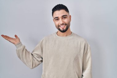 Soyutlanmış arka planda duran yakışıklı genç adam mutlu bir şekilde sunum yapıyor ve avuç içi kameraya bakıyor.. 