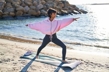 Deniz kenarında yoga eğitimi alan genç bir kadın.