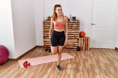 Genç kızıl saçlı kadın gülümsüyor spor merkezinde esniyor.