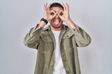 Tecrit edilmiş arka planda duran genç bir İspanyol dürbün gibi jest yapıyor, gözleri parmaklarından bakıyor. çılgın ifade. 