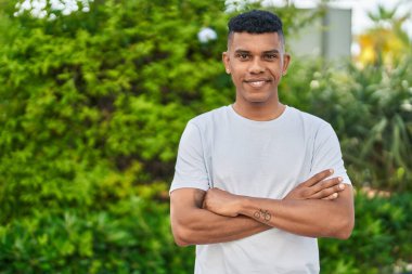 Young latin man smiling confident standing with arms crossed gesture at park