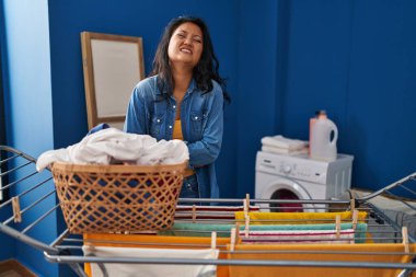 Young asian woman hanging clothes at clothesline with hand on stomach because nausea, painful disease feeling unwell. ache concept. 