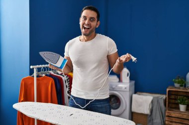 Sakallı genç İspanyol adam evde ütü yapıyor. Çılgınca kutlama yapıyor ve gözleri açık heyecanla haykırıyor.. 